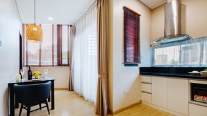 Cozinha moderna com piso de madeira, área de refeições com uma cadeira preta e uma janela grande com persianas.
