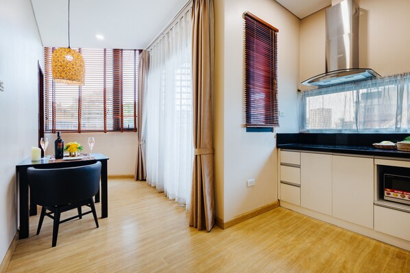 A modern kitchen with wooden flooring, a dining area with a black chair, and a large window with blinds.