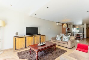 A living room with a wooden cabinet, a television, a sofa, and a red chair.