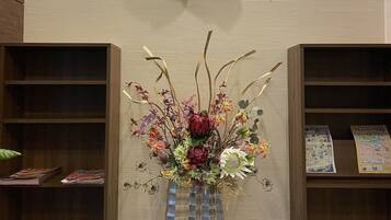 A reception desk with a decorative floral arrangement in a vase, wooden bookshelves, and a wall-mounted artwork.