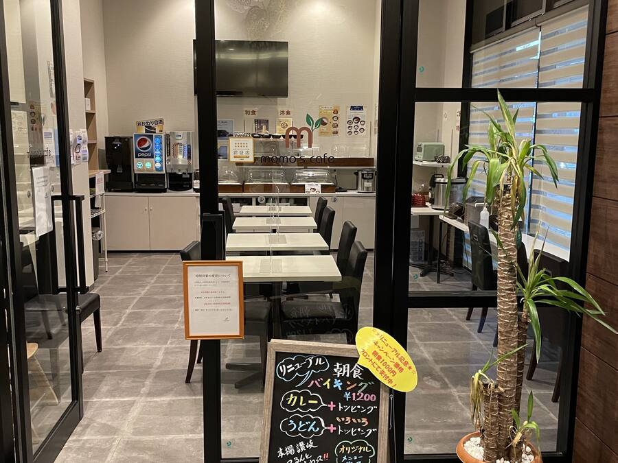 A cafe interior with tables, chairs, a chalkboard menu, and a potted plant.