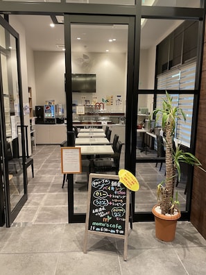 A cafe interior with tables, chairs, a chalkboard menu, and a potted plant. - Remington Hotel (Akashi)