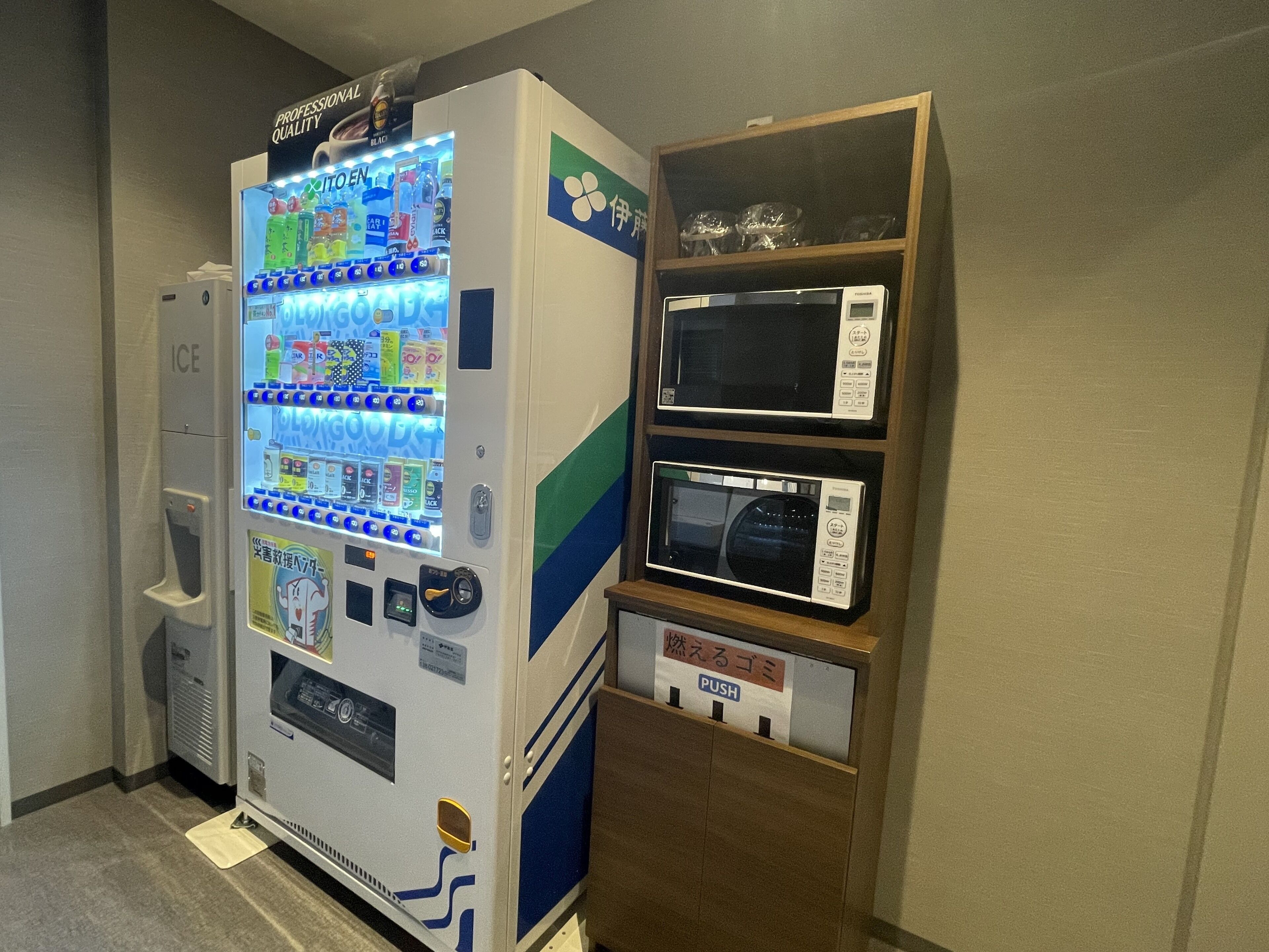 A vending machine with a selection of beverages and snacks, a microwave, and a small shelf with glassware.
