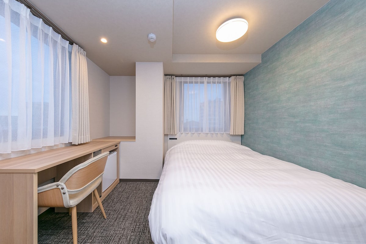 A hotel room with a bed, a desk, and a chair.
