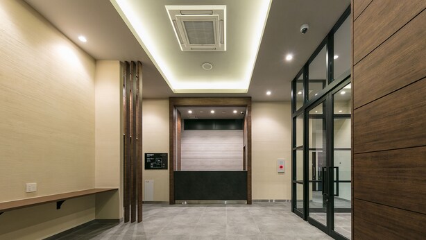 A modern hotel lobby with a tiled floor, a reception desk, a digital directory, and a glass elevator. - Remington Hotel (Akashi)