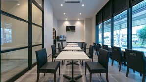 A modern conference room with tables and chairs, large windows, and a vending machine. - Remington Hotel (Akashi)