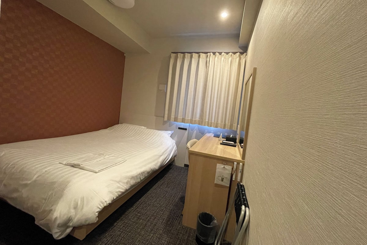 A hotel room with two single beds, a wooden desk, a mirror, and a window with curtains.