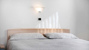 Una cama bien hecha con ropa de cama estampada, una lámpara de pared y un enchufe en la pared.