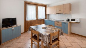 Una cocina compacta con una mesa de comedor, sillas, un televisor y un microondas.