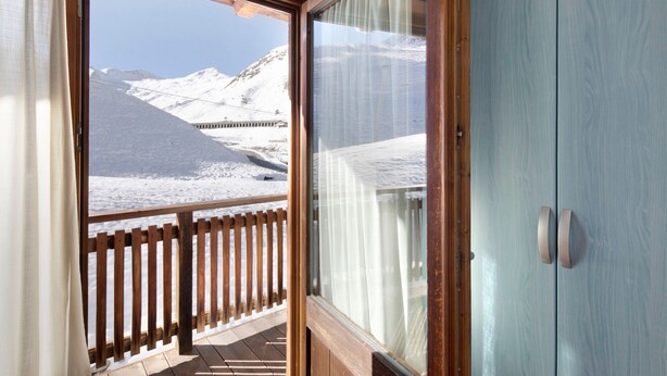 Una habitación con balcón de madera, puerta corrediza de vidrio y vistas a montañas nevadas.