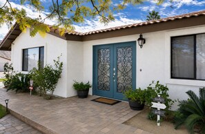 A house with a blue door, a window, and a potted plant in the front yard.