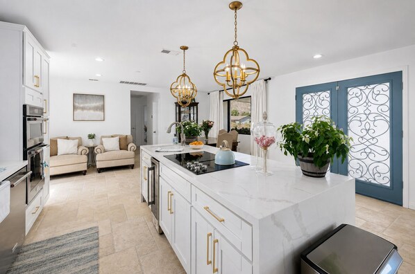 A modern kitchen with a central island, pendant lighting, and a view to the outside.