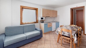 Een compacte woonruimte met een bank, een eettafel met stoelen, een kitchenette en een raam.