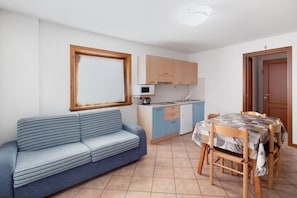 Een compacte woonruimte met een bank, een eettafel met stoelen, een kitchenette en een raam.