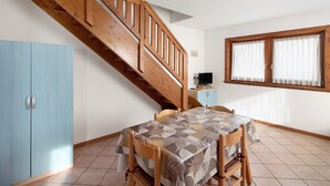 Een eetgedeelte met een tafel, stoelen, een houten trap, een raam met gordijnen en een blauwe kast.