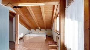 Een slaapkamer met een houten plafond, een bed, een stoel en een raam met gordijnen.