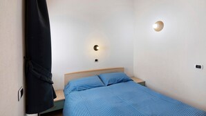 A bedroom with a single bed, a nightstand, a wall-mounted light, and a robe hanging on the wall. - Apartment "Bait del Pont 50" with Mountain View, Wi-Fi & Garden (Trepalle)