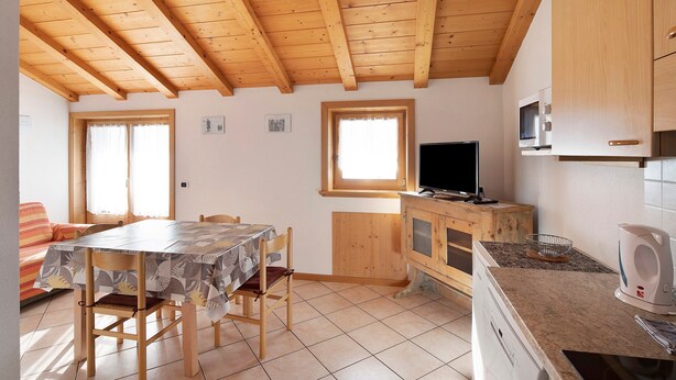 A kitchen with wooden beams, a dining table, chairs, a TV, and a microwave. - Apartment "Bait del Pont 50" with Mountain View, Wi-Fi & Garden (Trepalle)