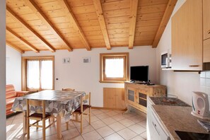 A kitchen with wooden beams, a dining table, chairs, a TV, and a microwave.