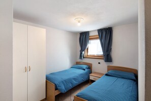 A bedroom with two single beds, a wardrobe, a window with curtains, and a ceiling light.