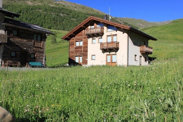 A two-story building with balconies, surrounded by a grassy field and hills.
