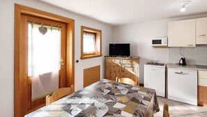 A compact room with a wooden door, a small window, a television, a microwave, a refrigerator, and a table with a patterned tablecloth. - Apartment "Bait del Pont 50" with Mountain View, Wi-Fi & Garden (Trepalle)