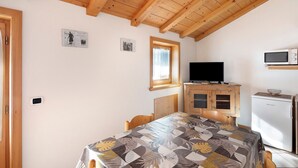 A room with a wooden ceiling, a television, a refrigerator, and a table with a patterned tablecloth. - Apartment "Bait del Pont 50" with Mountain View, Wi-Fi & Garden (Trepalle)