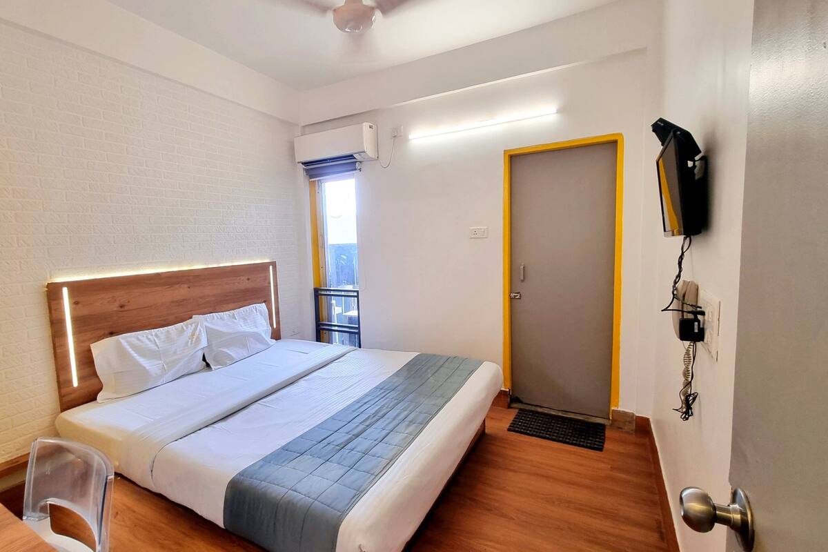 A hotel room with a bed, a desk, a chair, an air conditioning unit, a door, and a telephone.