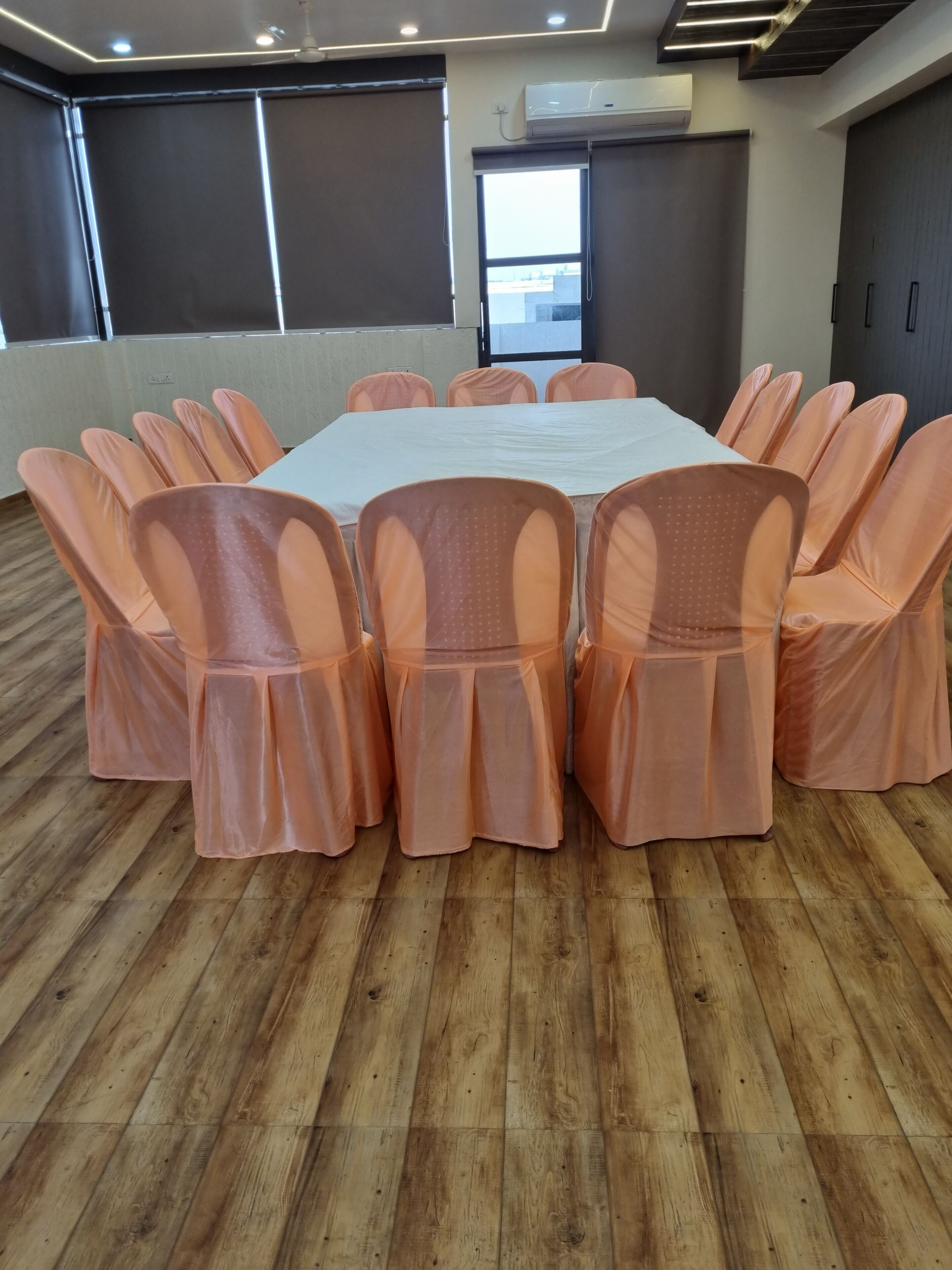 A conference room with a rectangular table, peach-colored chairs, wooden flooring, and large windows.