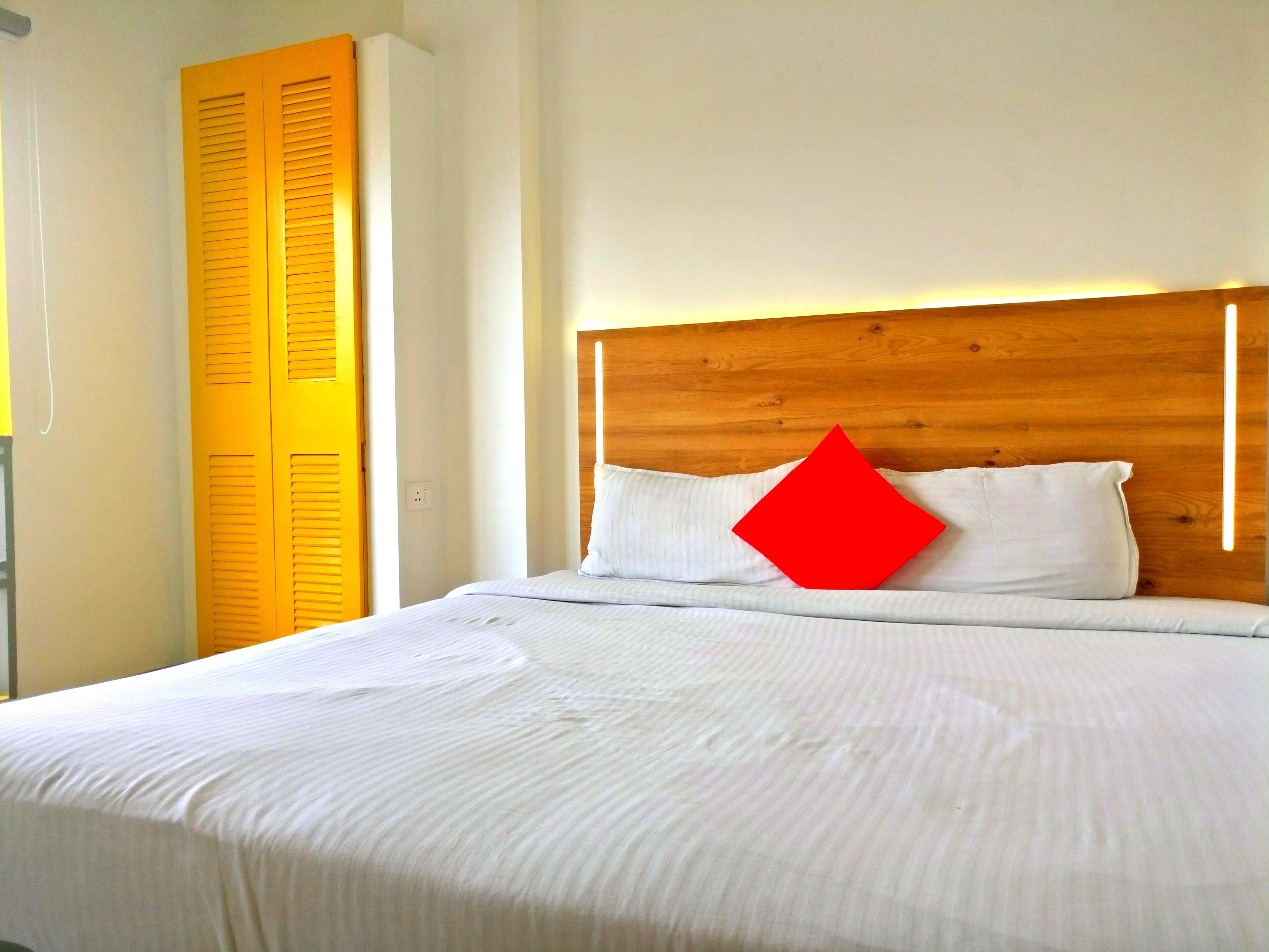 A bed with white bedding, a wooden headboard, and a red pillow.