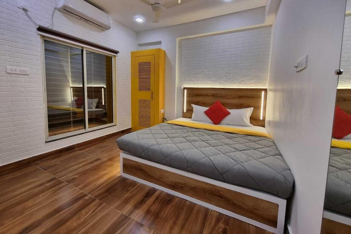 A bedroom with a bed, a window, a wardrobe, and an air conditioning unit.
