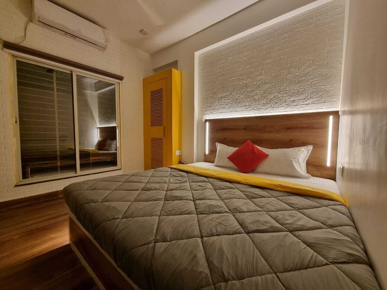 A bedroom with a large bed, a window with blinds, a wooden headboard, and a yellow door.