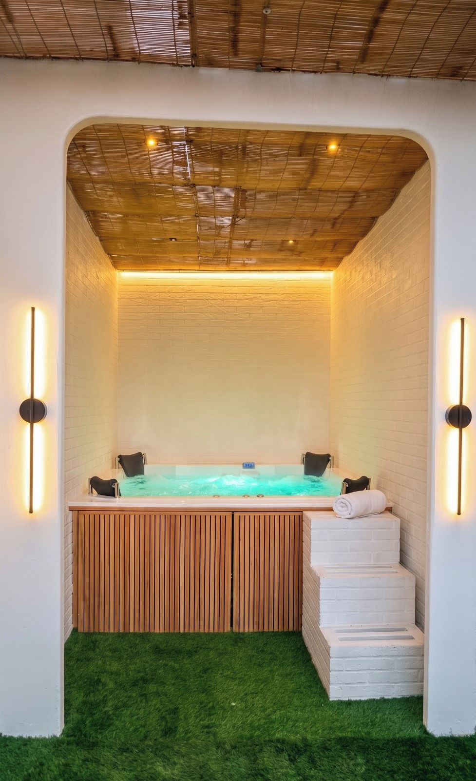 Un espace bien-être comprenant un jacuzzi, des marches en bois et des lampes fixées au mur.