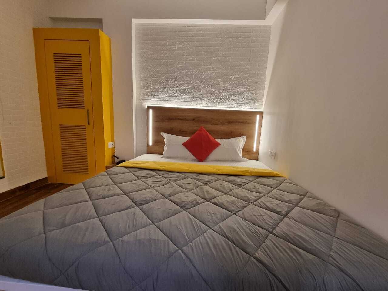 A bedroom with a bed, a window with blinds, a wooden door, and a white wall.