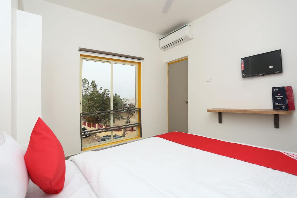 A hotel room with a bed, a window with a view, a mounted TV, and a small shelf.