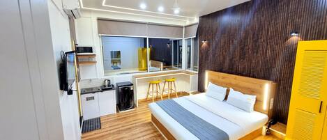 Una habitación de hotel moderna con una cama grande, una kitchenette, un pequeño comedor y vistas por la ventana.