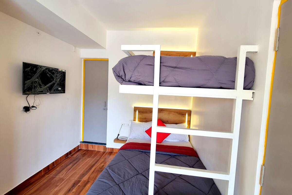 A bunk bed room with a television mounted on the wall, wooden flooring, and a door leading to another room.