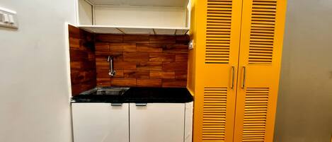 A compact kitchen with a sink, wooden backsplash, and a yellow cabinet.