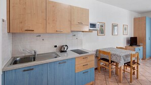 A kitchen with wooden cabinets, a sink, a microwave, and a dining area with a table and chairs. - Apartment "Bait del Pont 52B" with Mountain View, Wi-Fi & Garden (Trepalle)