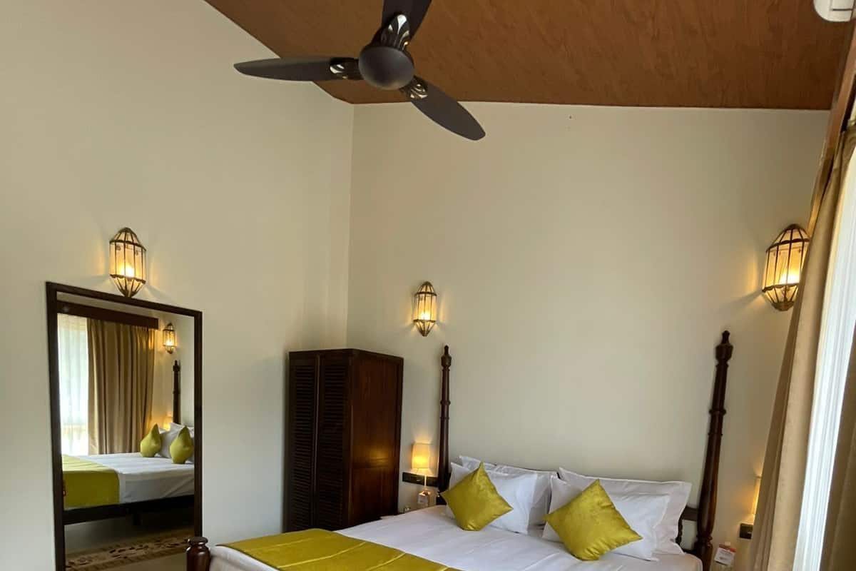 A hotel room with a bed, a ceiling fan, a mirror, and wall-mounted lights.