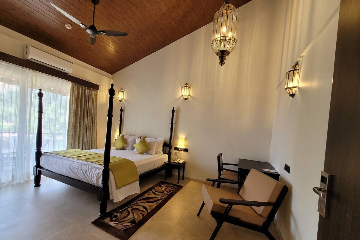 A bedroom with a four-poster bed, a desk, a chair, a standing lamp, and a ceiling fan.