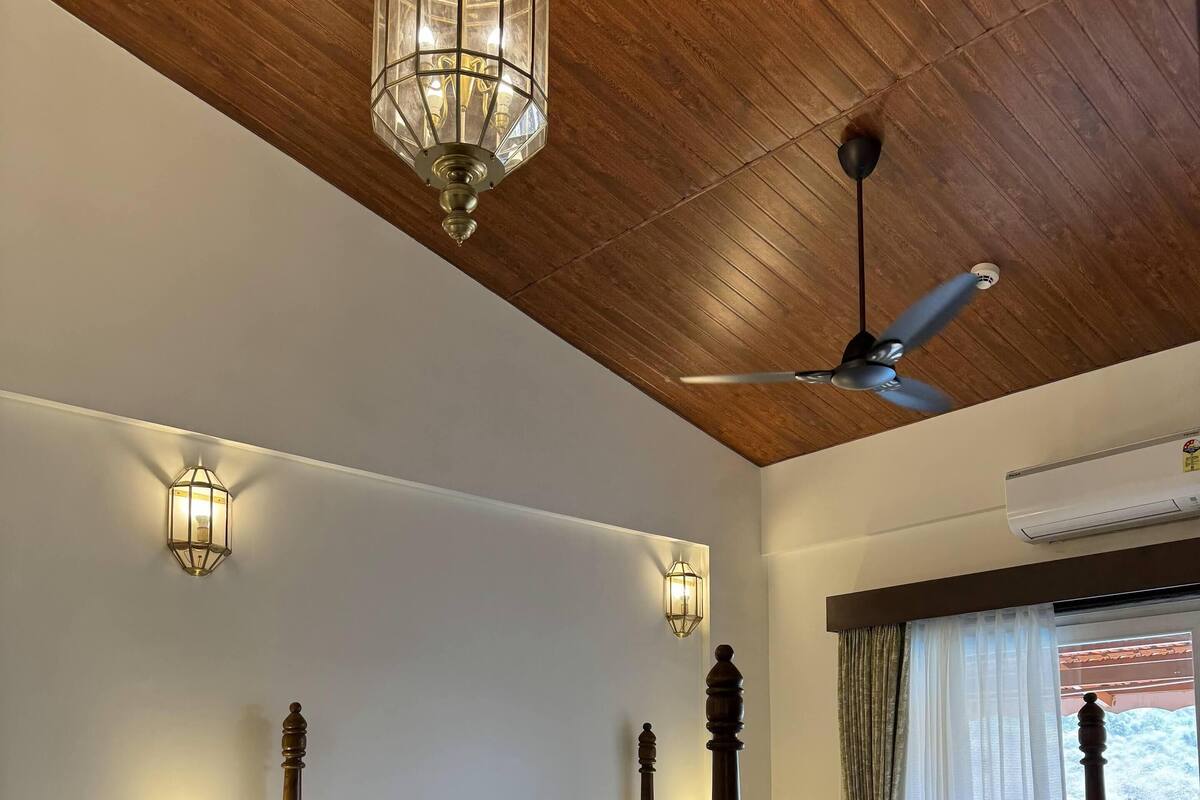 A four-poster bed with a wooden frame, two bedside tables, a ceiling fan, and two wall-mounted light fixtures.