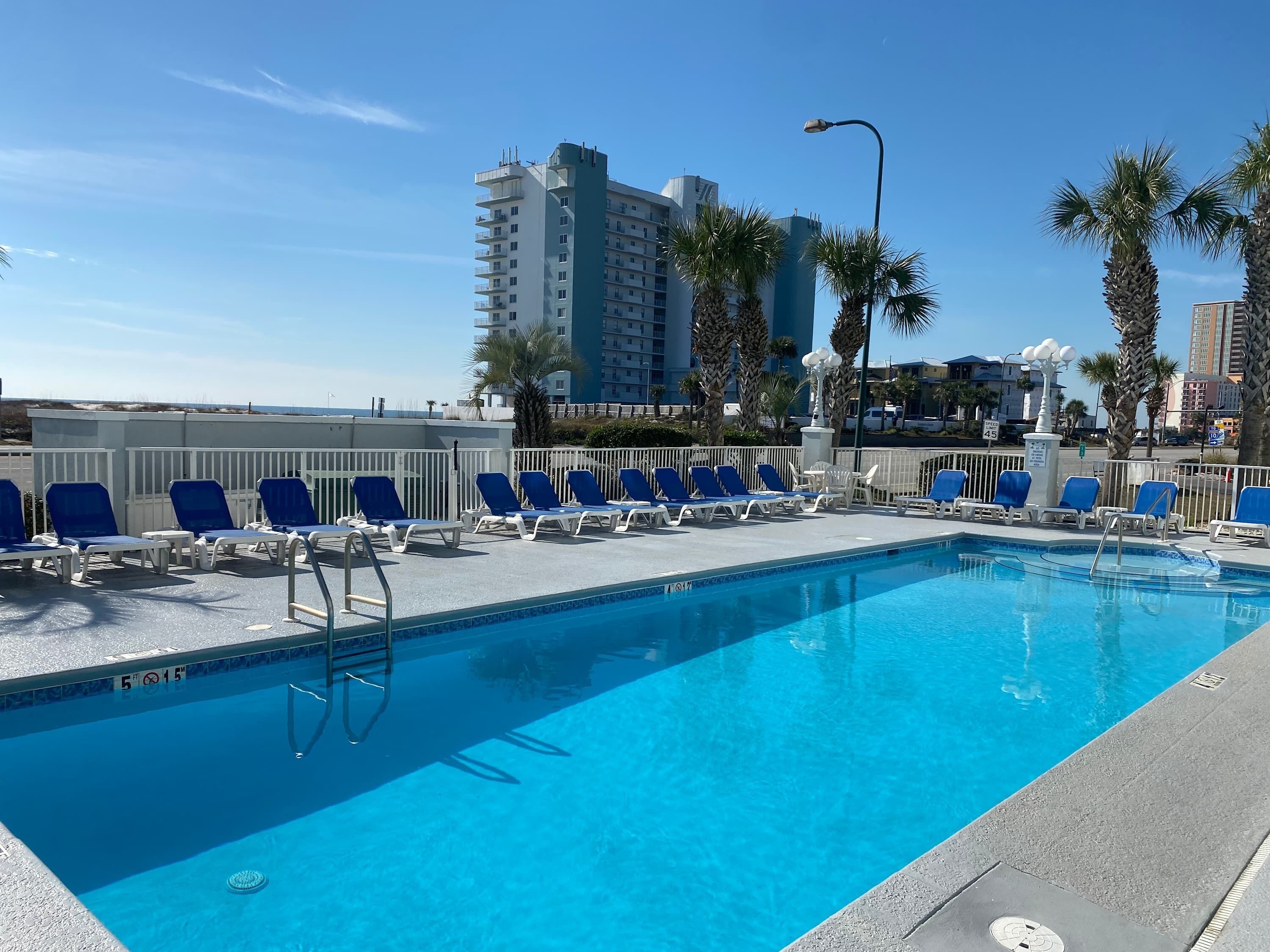 A pool area with blue lounge chairs and a clear blue pool.