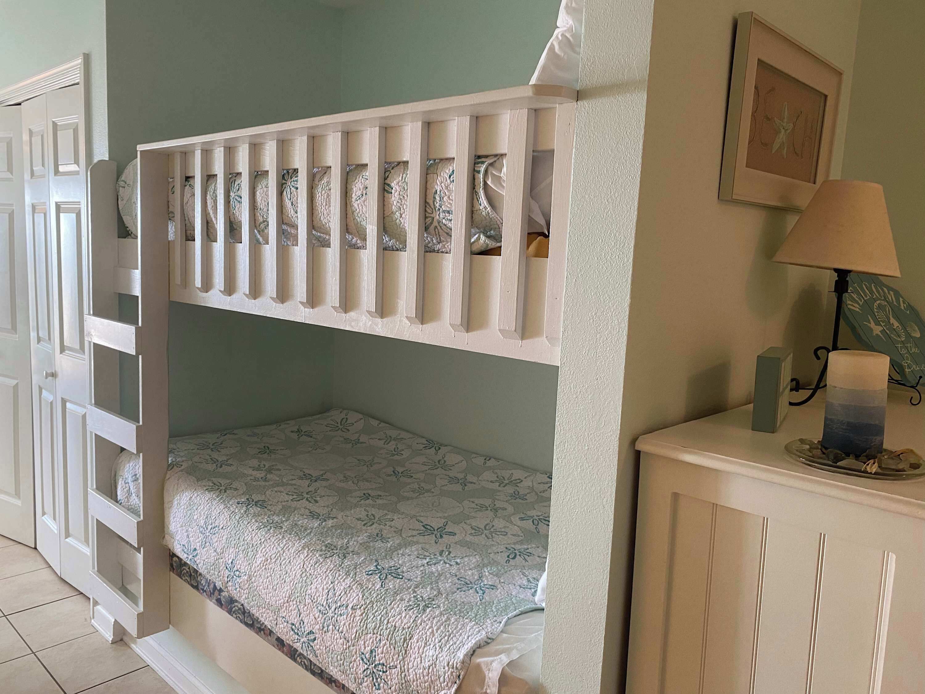 A bunk bed with a patterned bedspread, a bedside lamp, and a framed picture on the wall.