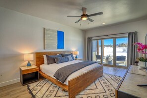 A bedroom with a wooden bed, a ceiling fan, a large window with a view of a snowy landscape, and a nightstand with a lamp.
