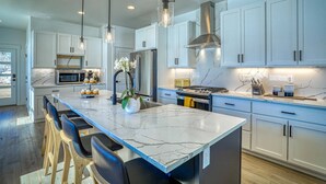 Una cocina moderna con encimeras de mármol, electrodomésticos de acero inoxidable e iluminación colgante.