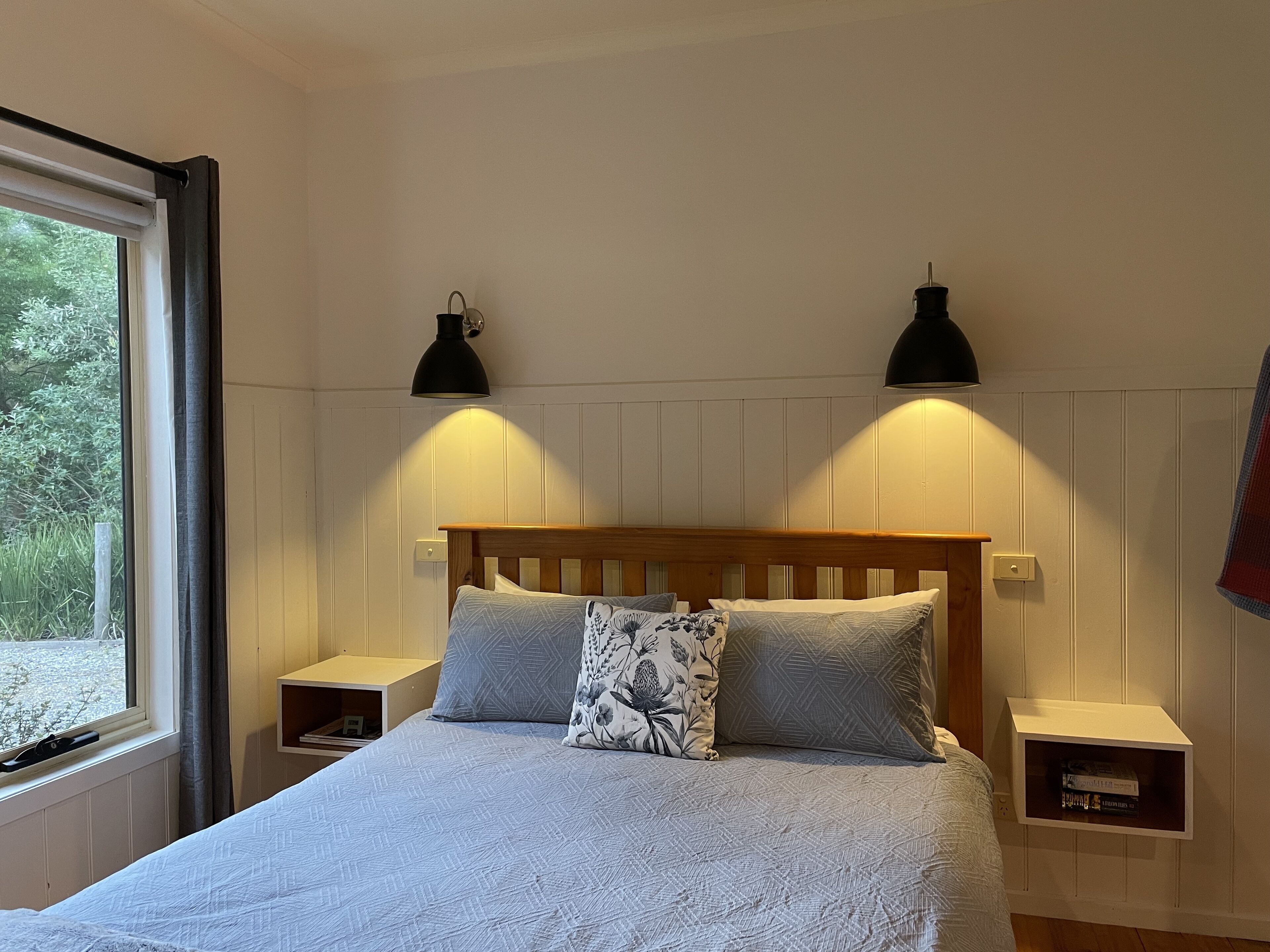 Un dormitorio con cabecera de madera, dos mesitas de noche, una cama con ropa de cama estampada y dos lámparas fijadas a la pared.