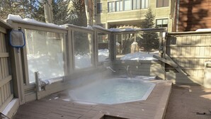 A hot tub with a wooden deck, surrounded by a wooden fence and a stone wall. - Cozy condo, Ski-in, one block from Main Street (Breckenridge)