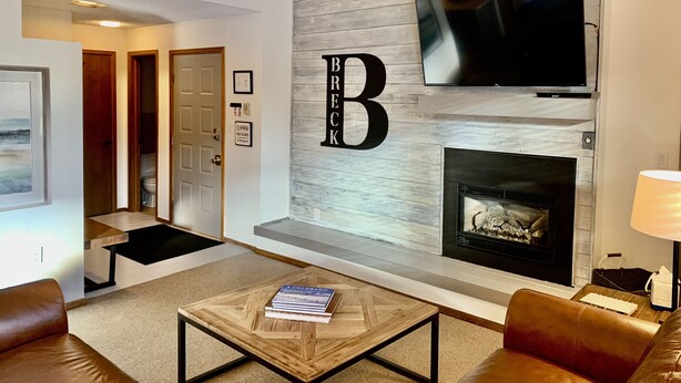 A modern living room with a fireplace, a mounted TV, and a coffee table with books. - Cozy condo, Ski-in, one block from Main Street (Breckenridge)