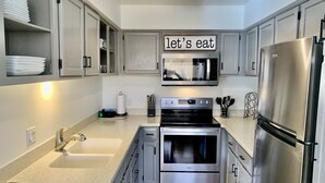A modern kitchen with stainless steel appliances, a microwave, and a sign that reads "let's eat". - Cozy condo, Ski-in, one block from Main Street (Breckenridge)